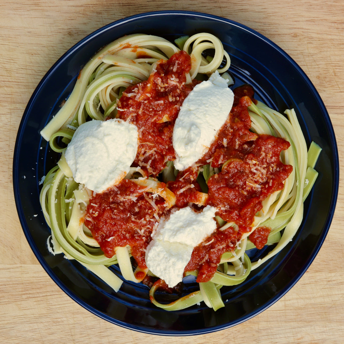 Plate of spaghetti with tomato sauce and ricotta cheese on a wooden table