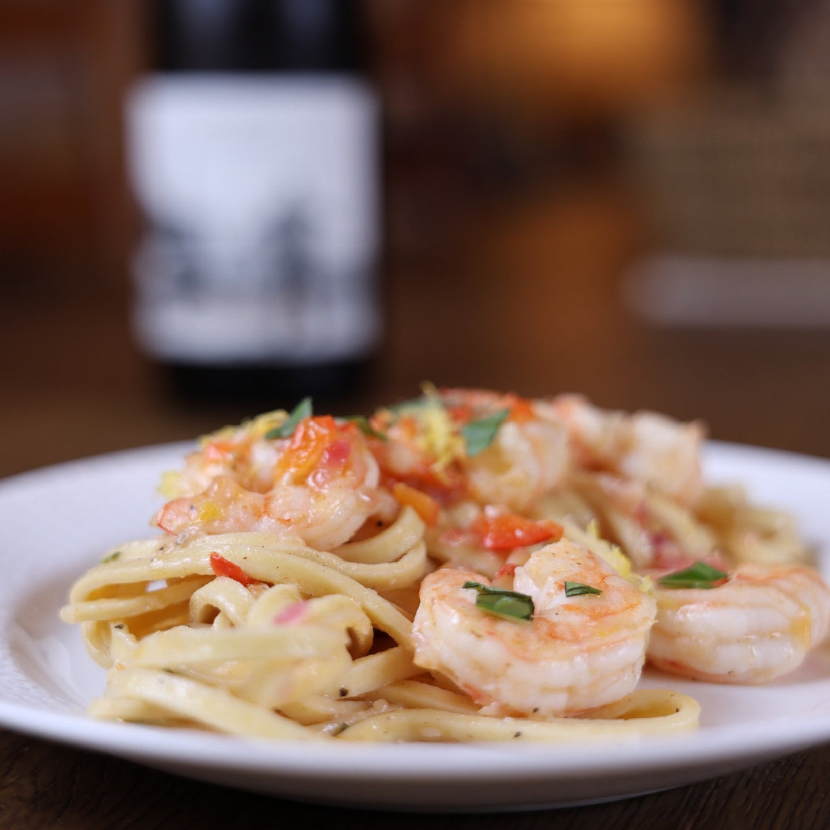 Plate of Fettuccine with shrimp on a wooden table with a blurred bottle in the background