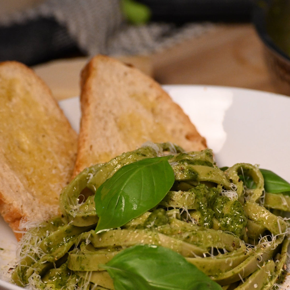 Pasta dish with green sauce and basil leaves served with bread on a wooden table.