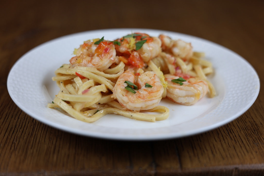 Pasta dish with shrimp on a white plate on a wooden table