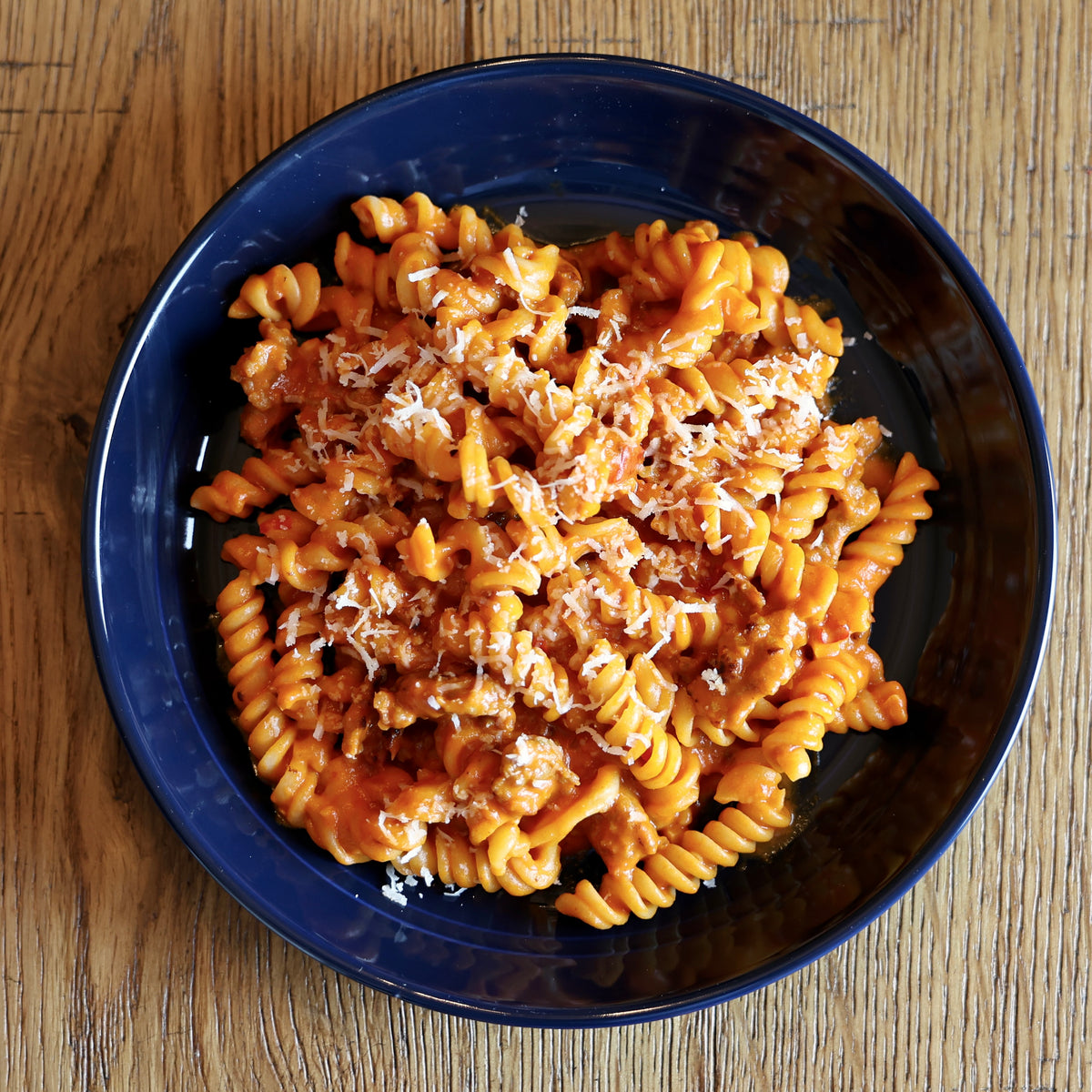 Fusilli dish with tomato sauce and parmesan cheese in a blue bowl on a wooden table