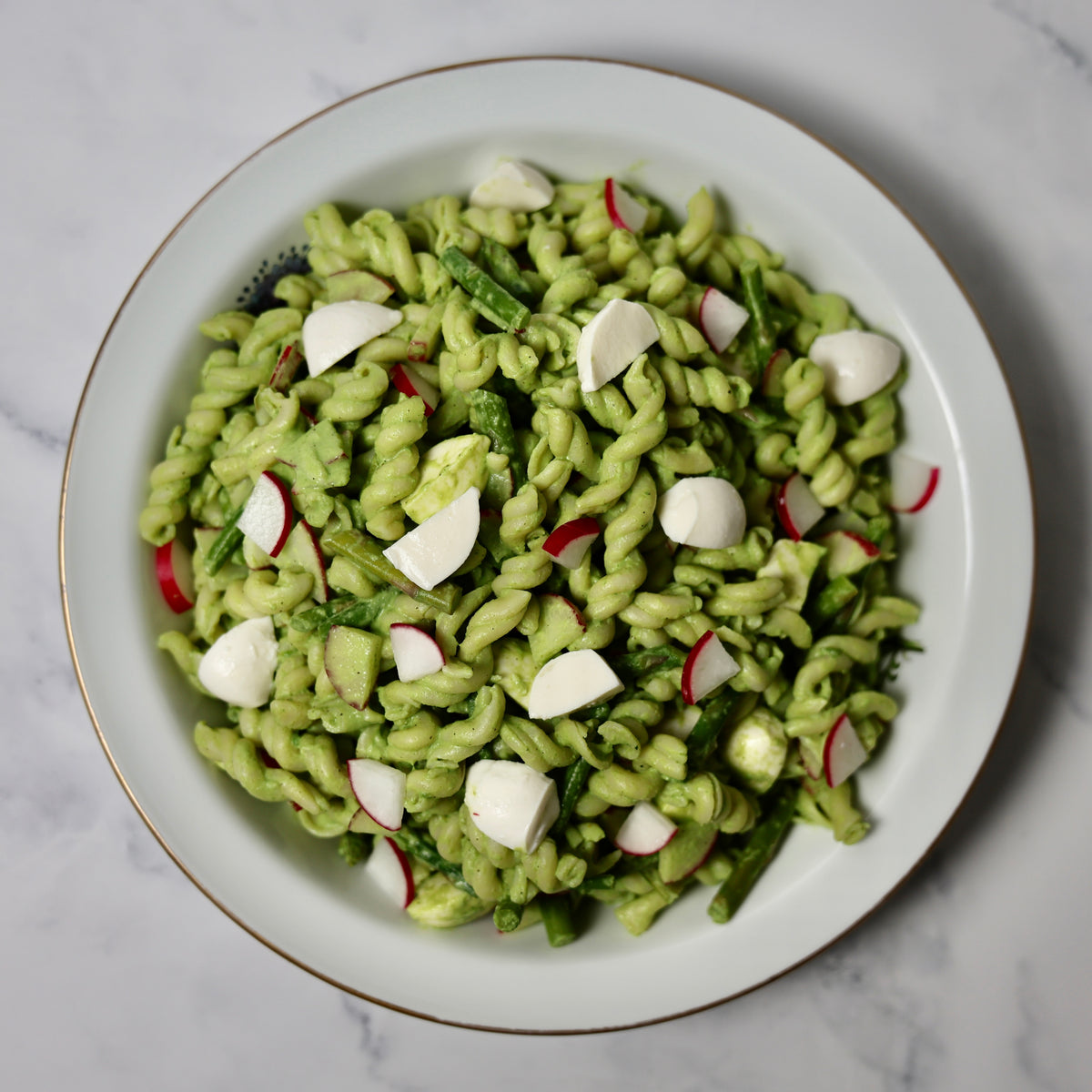 Green pasta salad with radishes on a white plate