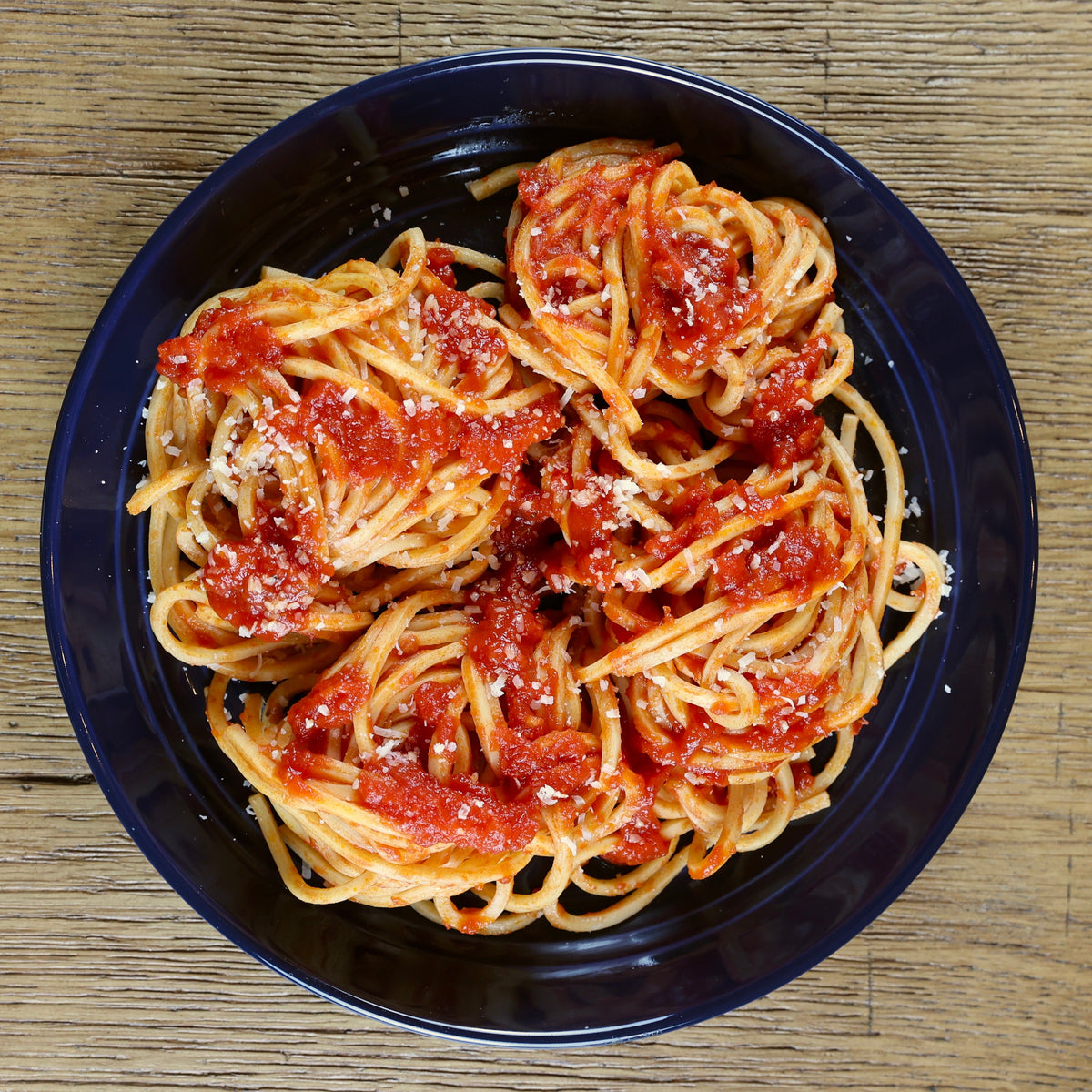 Linguine with tomato sauce in a black bowl on a wooden table