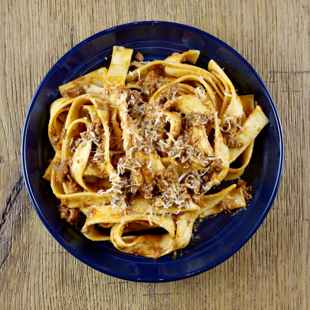 Pappardelle Bolognese and cheese on a blue plate on a wooden table
