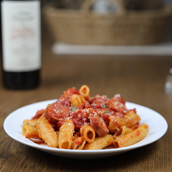Plate of rigatoni with red sauce on a wooden table with a bottle in the background