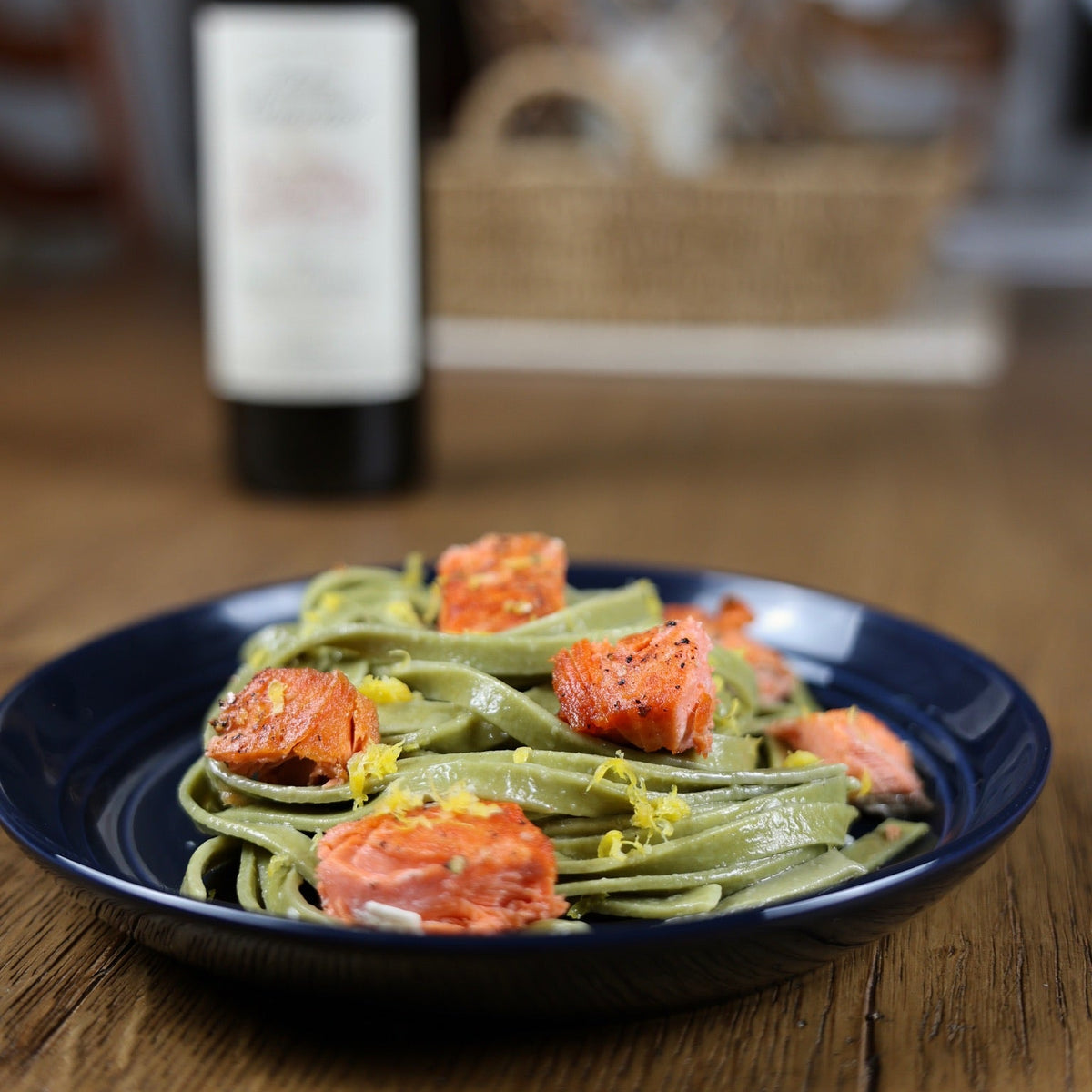 Plate of green pasta with salmon on a wooden table with a blurred background