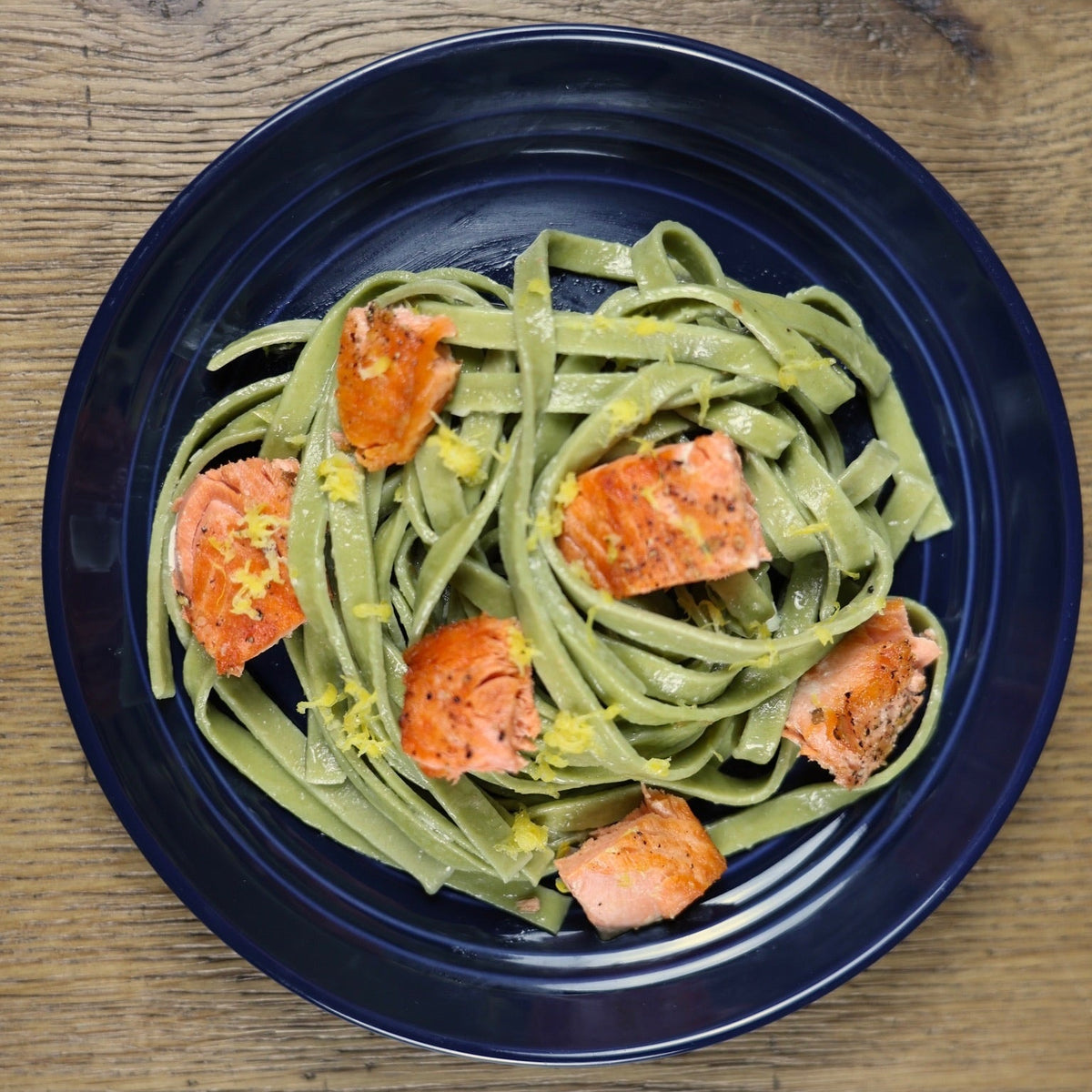 Green pasta with salmon pieces on a dark blue plate on a wooden table
